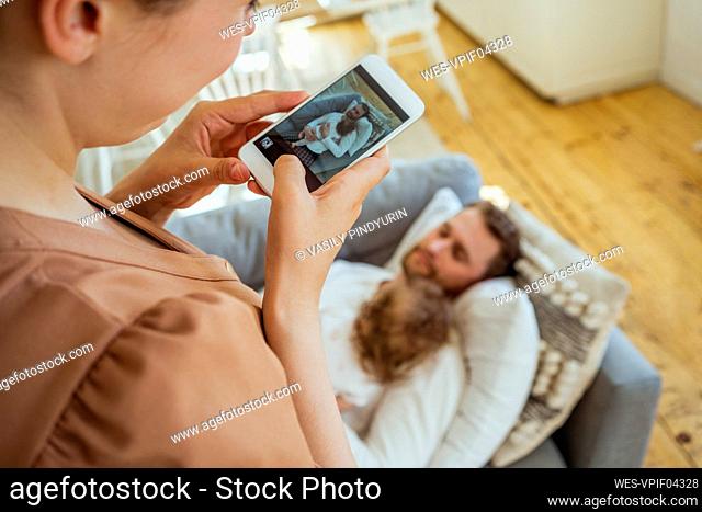 Woman photographing man with daughter sleeping on sofa at home