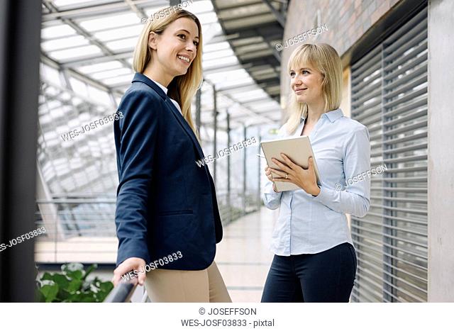 Two happy young businesswomen with tablet in modern office building