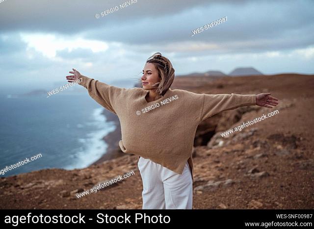 Carefree woman looking away while standing with arms outstretched on mountain at Famara Beach, Lanzarote, Spain