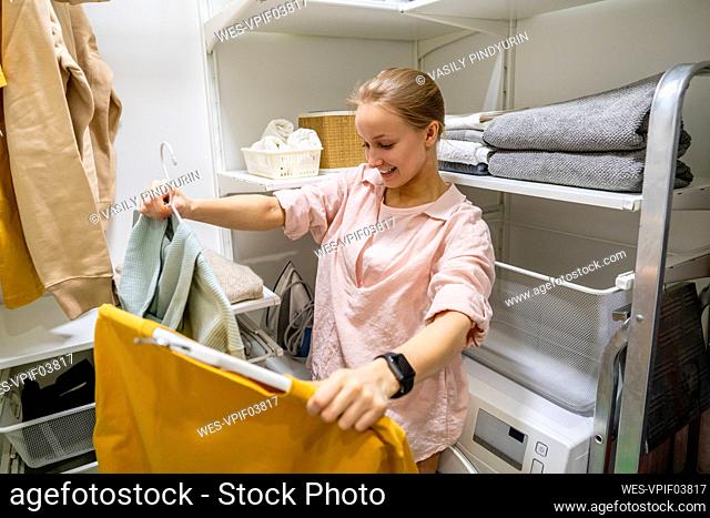 Smiling woman looking at clothes while standing in utility room