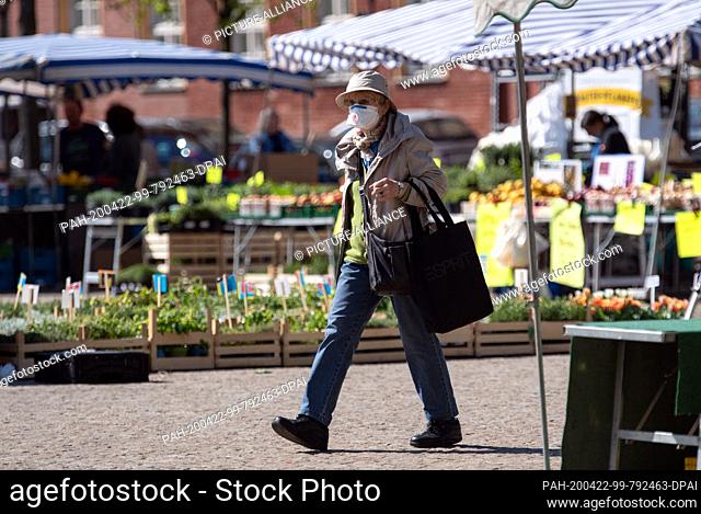 22 April 2020, Brandenburg, Potsdam: A woman with a shopping bag and mouth guard walks through the weekly market in the city centre