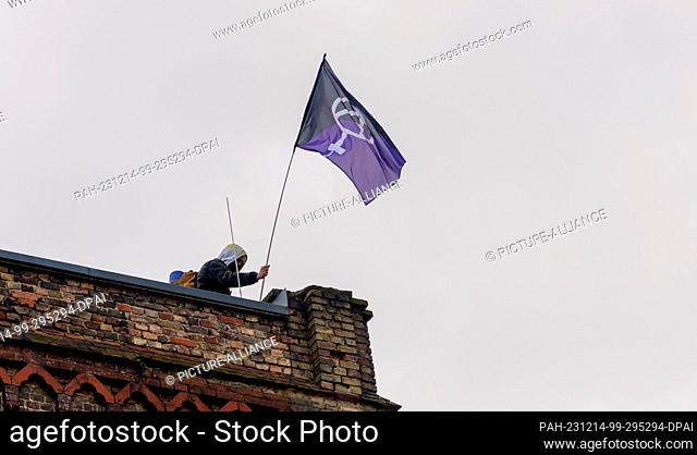 14 December 2023, Hesse, Frankfurt/Main: An activist stands with a flag on the roof of the Dondorf printing works. On Thursday morning