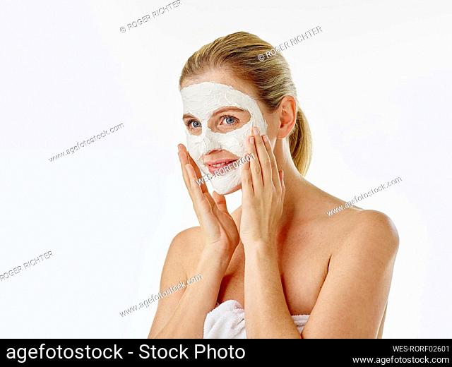 Smiling woman wrapped in towel applying face mask