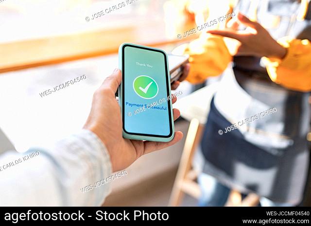 Man holding mobile phone showing check mark on screen at cafe