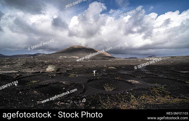 Male tourist with arms outstretched standing on black volcano ash at El Cuervo Volcano, Lanzarote, Spain