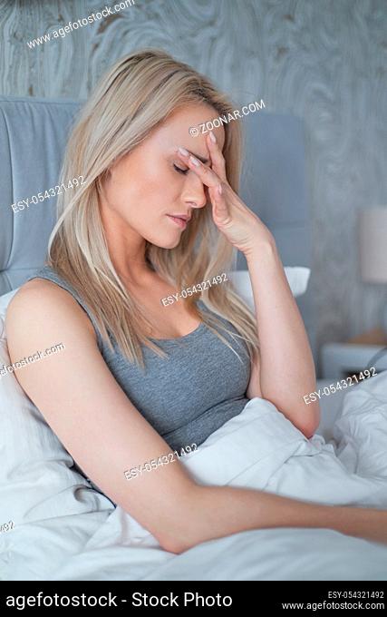 Women sitting on bed holding her head. She has a painful headache with migraine