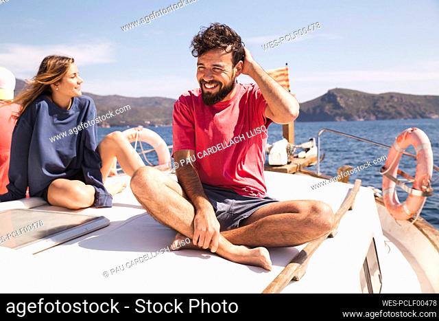 Smiling man sitting cross-legged by woman on yacht at vacation