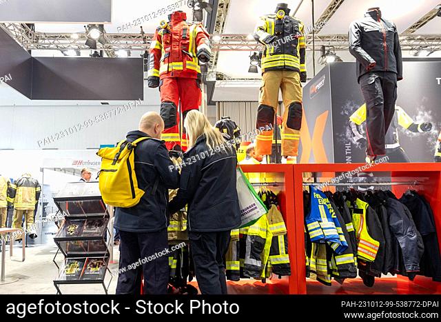 12 October 2023, Saxony, Dresden: A man and a woman look at the clothing offerings of exhibitor Texport at the ""Florian 2023"" firefighting trade show in the...