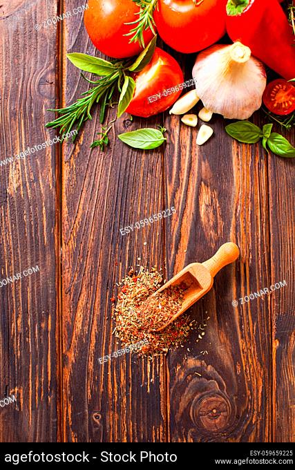 Top view of the wooden scoop with spices and fresh vegetables arranged above on the wooden table with place for copyspace
