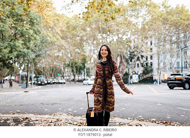 Portrait happy female tourist with suitcase on urban autumn street