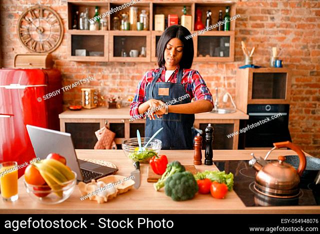 Black woman in apron cooking healthy breakfast on the kitchen. African female person preparing vegetable salad at home