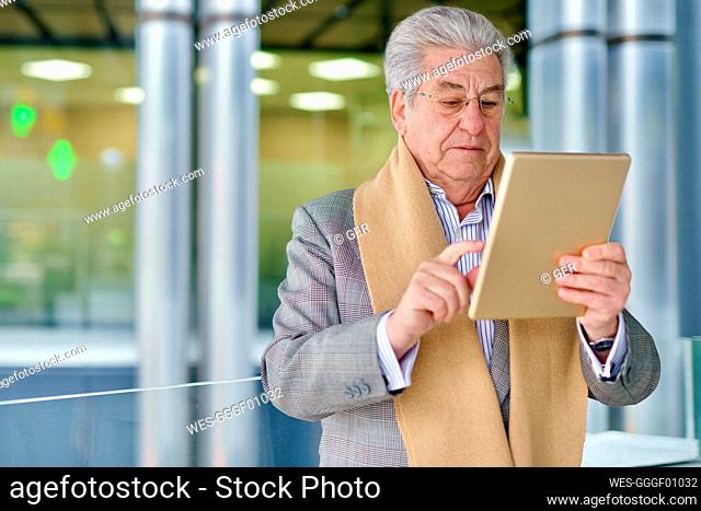 Senior businessman using tablet PC in front of glass wall