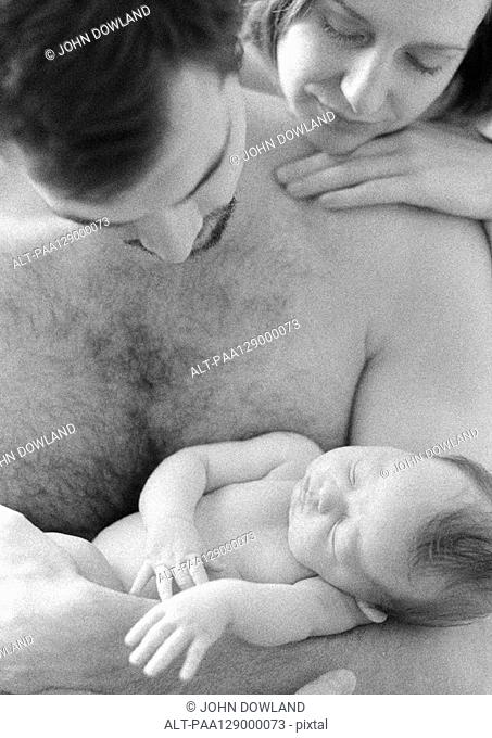 Father holding sleeping infant, mother looking over father's shoulder, b&w