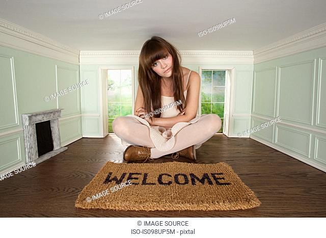 Young woman sitting in small room with welcome mat