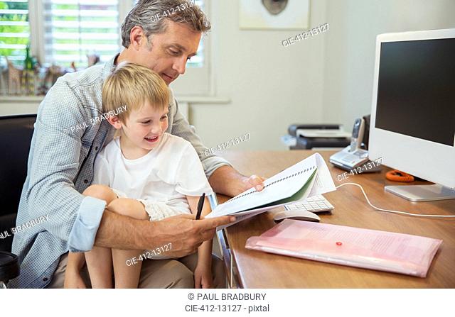 Son sitting on working father's lap