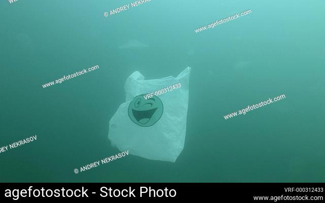 Plastic pollution, used white plastic bag with green smiley slowly drifts underwater. Plastic debris underwater. Plastic garbage environmental pollution problem