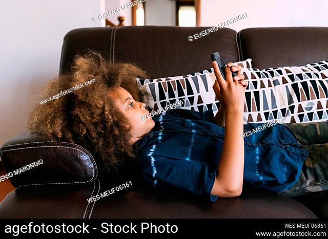 Boy using smart phone lying on sofa at home