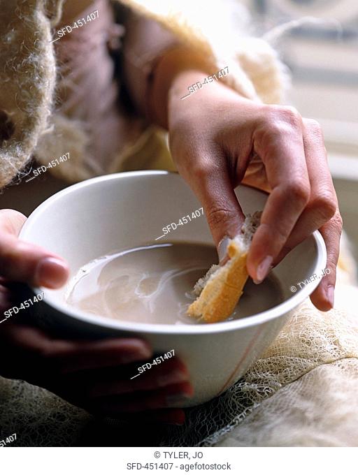 A hand dipping bread into a bowl of coffee