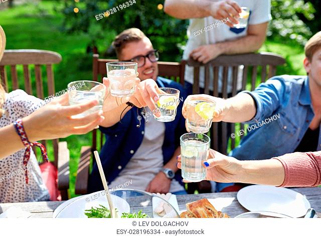 leisure, holidays, eating, people and food concept - happy friends having dinner at summer garden party and clinking drinks