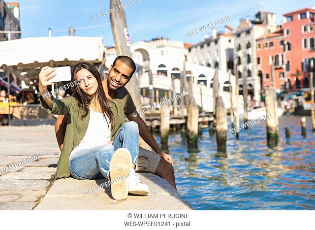 Italy, Venice, couple relaxing and taking a selfie with Rialto bridge in background