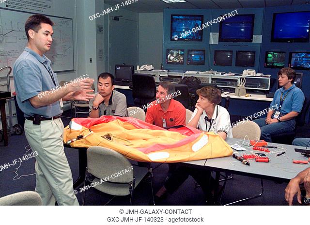 The STS-114 crewmembers are briefed by United Space Alliance (USA) crew trainer Adam G. Flagan (standing) during a classroom session preceding water survival...