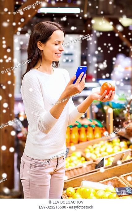 sale, shopping, consumerism and people concept - happy young woman with smartphone and tomato in market over snow effect