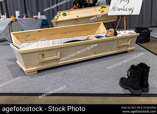 21 October 2022, Baden-Württemberg, Freiburg: Natascha Gmür lies in a coffin at the fair ""Life and Death"" sample, while in the foreground her shoes can be...