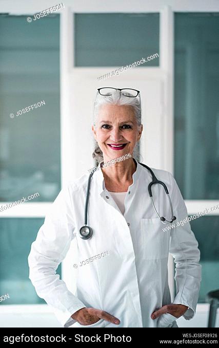 Happy doctor wearing stethoscope standing with hands in pockets