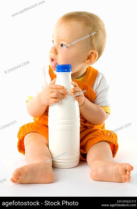 Little baby boy sitting on the floor and holding a bottle of milk. Whole body, front view