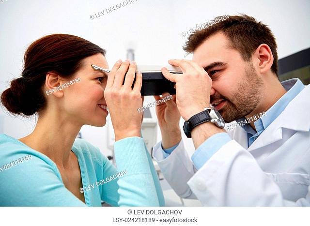 health care, medicine, people, eyesight and technology concept - optometrist with pupilometer checking patient intraocular pressure at eye clinic or optics...