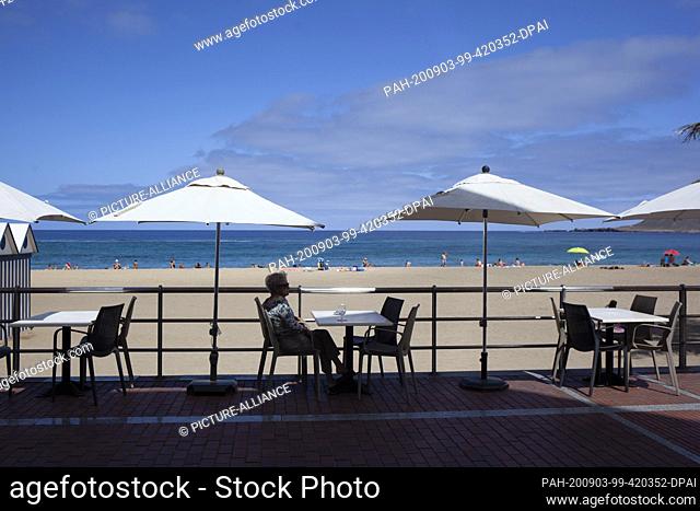 03 September 2020, Spain, Las Palmas de Gran Canaria: A woman takes a drink on the terrace of a bar on the beach in Las Palmas de Gran Canaria