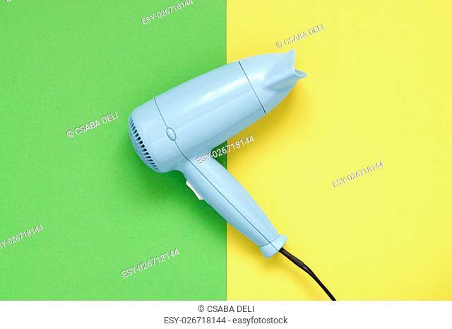 Blue hair dryer on green and yellow paper background
