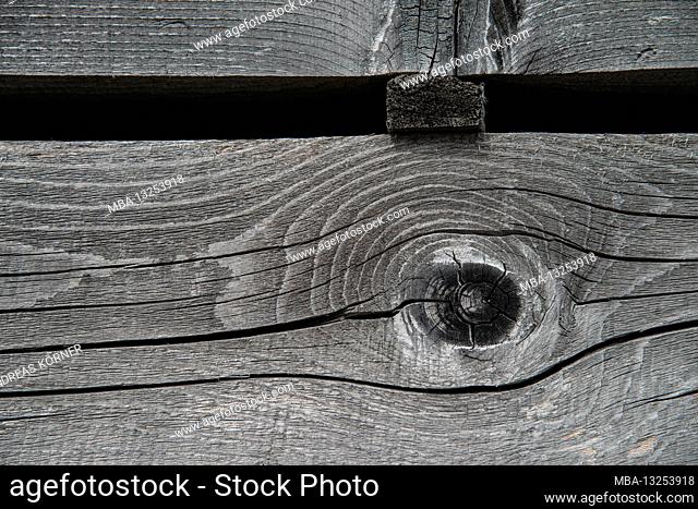 Faded, parallel wooden slats with knotholes in front of a black background