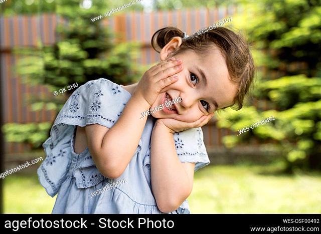 Playful girl standing with head in hands at back yard
