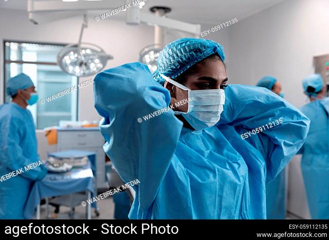 Mixed race female doctor putting on face mask standing in operating theatre