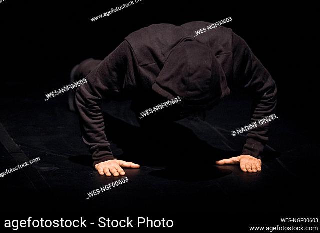 Dancer wearing black hood crouching on stage