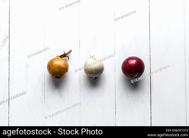 Three bulbs on a white wooden background. White onions, onions and red onions. Top view