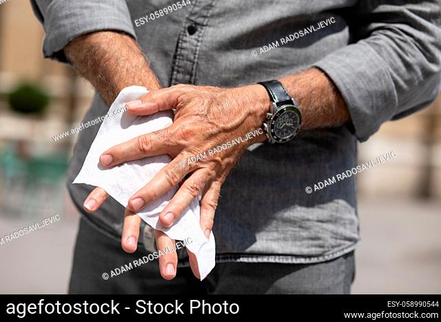 Old man cleaning hands with wet wipes, white