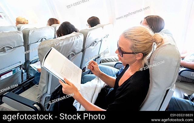 Female traveler reading magazine on airplane during flight. Female traveler reading seated in passanger cabin