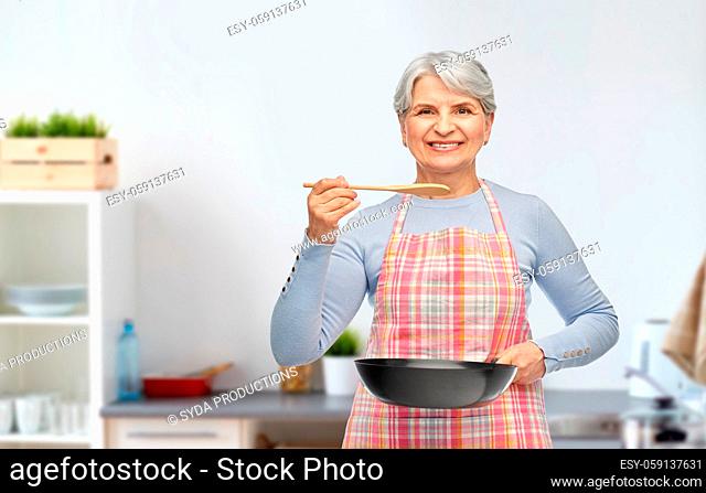 smiling senior woman with frying pan at kitchen
