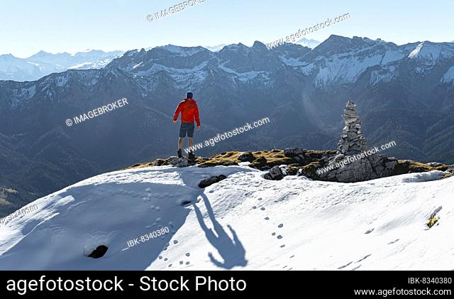Mountaineer next to a cairn, in front of snowy mountains of the Rofan, hiking trail to the Guffert with first snow, in autumn, Brandenberg Alps, Tyrol, Austria