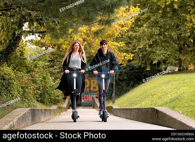 Trendy fashinable teenagers riding public rental electric scooters in urban city park. New eco-friendly modern public city transport in Ljubljana, Slovenia