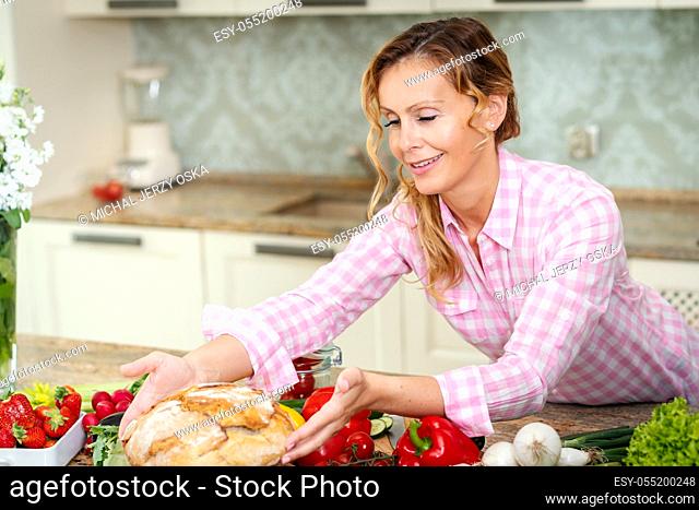 woman at the table with vegetables holds fresh and fragrant bread in her hands