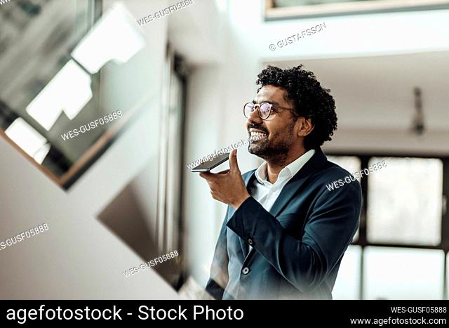 Smiling male professional talking through speaker on smart phone in office