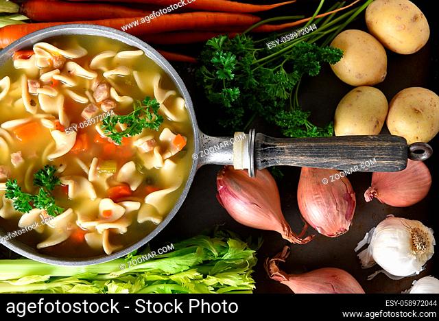 A pot of fresh homemade Chicken Noodle Soup surrounded by some of the ingredients
