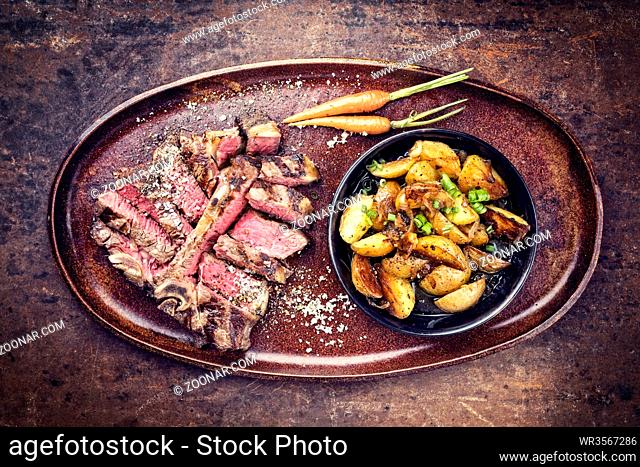 Barbecue dry aged wagyu porterhouse steak sliced with fried potatoes as top view on a plate