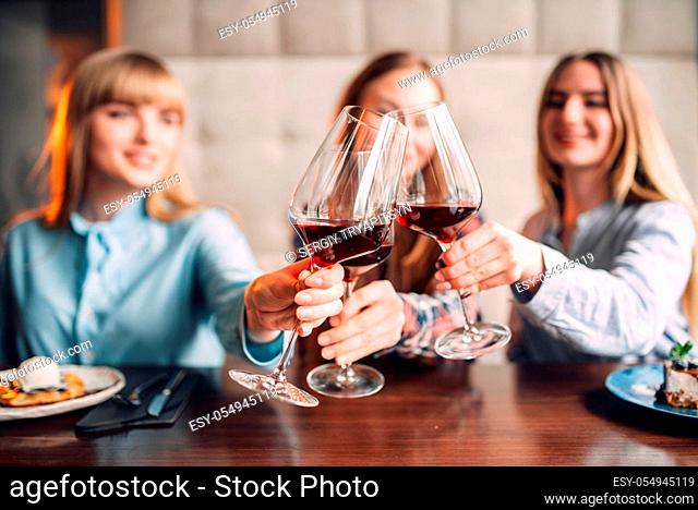 Portrait of three girlfriends holding beverages in glasses. Young women celebrate event in cafe