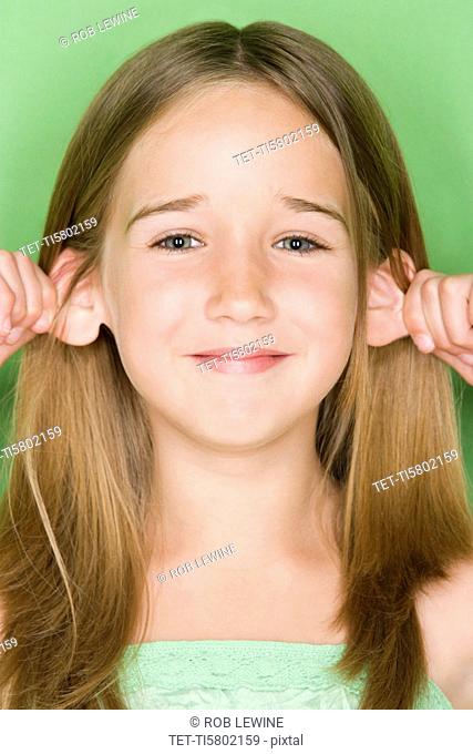 Studio shot portrait of teenage girl pulling her ears, close-up