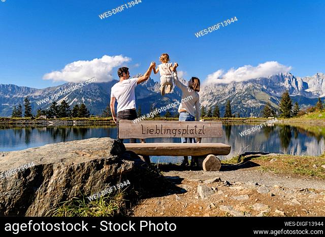 Family with one little daughter standing together behind lakeshore bench in Kaiser Mountains