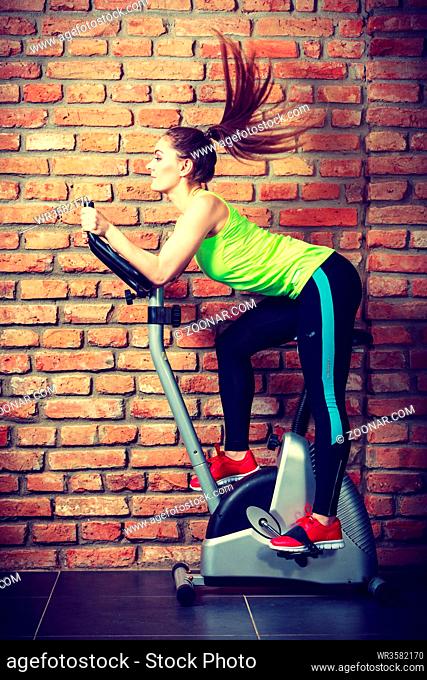 Active young woman working out, doing sport biking in the gym for fitness. Sporty girl training in club. Slim body weight loss concept